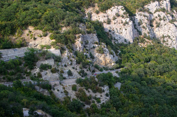 Winding road on the slope of a mountain range with a green forest.