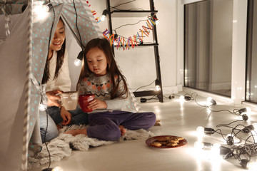 Asian woman with her daughter little girl sitting on floor with cookies and cocoa. Christmas concept.