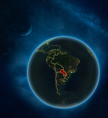 Paraguay at night from space with Moon and Milky Way. Detailed planet Earth with city lights and visible country borders.