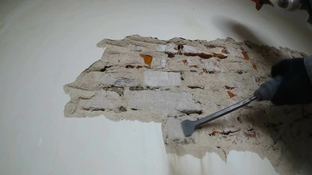 worker in protective suit demolishes plaster wall. Punch and falling plaster close-up.