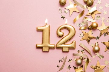 Number 12 gold celebration candle on star and glitter background
