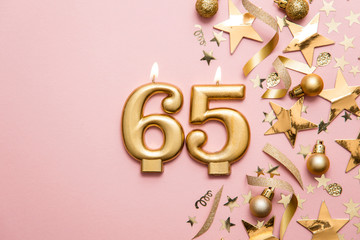Number 65 gold celebration candle on star and glitter background