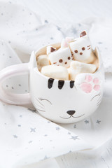 Mug with hot chocolate and melted marshmallows in the shape of cats, kittens