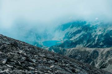 Beautiful foggy alpine high mountains peaks, lake, summertime.