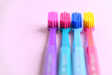 Four  multicolored toothbrushes with selective focus on pink background. Toothbrush for personal routine morning  hygiene on neutral backdrop. Dental plastic tool with empty space for image or text