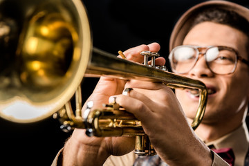 Obraz premium selective focus of male jazzman in hat and eyeglasses playing on trumpet isolated on black