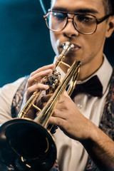 Obraz premium selective focus of young jazzman playing on trumpet on stage with dramatic lighting and smoke