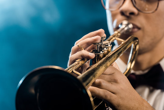 cropped shot of male musician playing on trumpet on stage with dramatic lighting and smoke