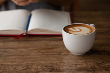 Woman checking her work on smart-phone blurred on background with warming drink, Late coffee in a cup in front-of on wooden table on-line working concept design