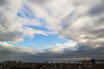 Dramatic cloudscape over the seaside city. Dark clouds surround the last spot of a blue sky in a daytime
