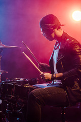 Fototapeta na wymiar side view of male musician in leather jacket playing drums during rock concert on stage with smoke and dramatic lighting