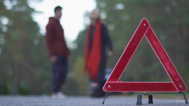 Two people swear on a background of warning triangle. Silhouette of swearing couple. Focus on car sign.