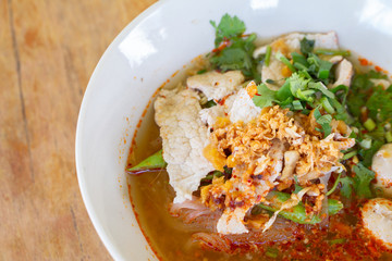 Rice noodle in spicy soup with pork ball, vegetable and pork serving on wooden desk in canteen