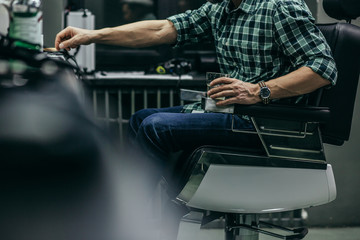 Close up of man sitting in barber chair and holding alcohol