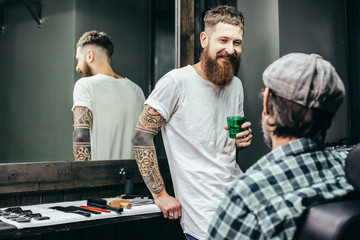 Waist up of positive barber smiling to his client in barbershop