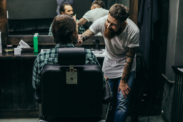 Positive bearded barber smiling and carefully brushing beard of client