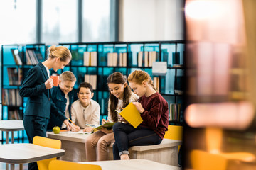 selective focus of schoolchildren and librarian reading books together in library