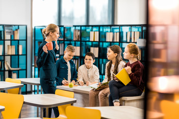 young female librarian and schoolkids talking together in library