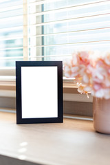 Blank black color picture frame template for place image or text inside on the desktop table work space with laptop and flower. window light