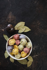 Bowl of raw multicolored dumplings or pelmeni over dark brown stone background, flatlay, copy space