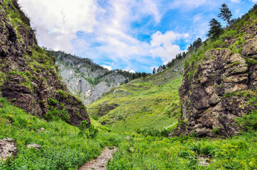 Fototapeta na wymiar Magnificent summer mountain landscape, Altai mountains, Russia - path leading into the stony bag, formed by steep cliffs. Brook flowing under rock, clouds on blue sky and majestic beauty of nature