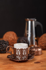 Richly decorated small traditional Turkish embossed copper Cup for strong black coffee on wooden background with metal coffee pot. The concept of coffee for the cafe.
