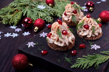 Canape shaped as a Christmas tree with pate garnished with pomegranate and dill surrounded by Christmas decorations