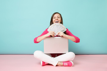 Full length portrait of young woman in rose shirt blouse, white pants sitting on floor hold money...