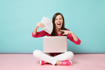 Full length portrait of young woman in rose shirt blouse, white pants sitting on floor hold money...