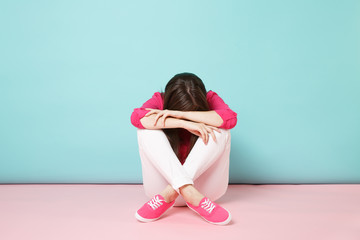 Full length portrait of sad upset young woman in rose shirt blouse, white pants sitting on floor...