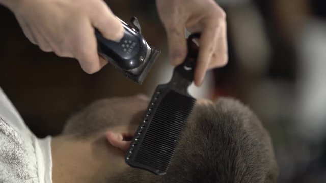 Male barberman hands cutting hair of a man with the hairclipper using comb. Vertical format. Beaty and style concept