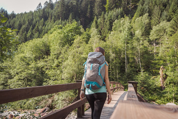 Fototapeta na wymiar woman with a backpack walking on a bridge into the forest