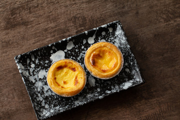 Egg tarts in aluminum foil cup on wood table,  traditional Portuguese dessert served in coffee shop