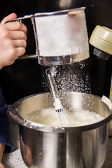 Fototapeta na wymiar Iron bowl with dough in which flour is poured through a sieve