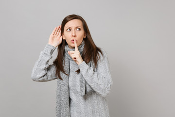 Young girl in gray sweater scarf saying hush be quiet with finger on lips shhh gesture eavesdrop...