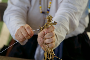 An elderly woman makes a toy for child in the form of a straw man. Traditional Russian folk art
