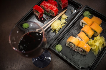 Almost eaten Japanese rolls, packed in plastic containers for the transport of fast food and a glass of red wine. Focus on meal