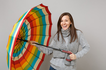 Laughing young woman in gray sweater, scarf holding colorful umbrella isolated on grey background...