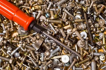 Screwdriver on the background of bolts, nuts, washers, screws and small iron parts.