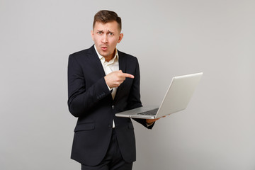 Perplexed young business man in classic black suit, white shirt pointing index finger on laptop pc...