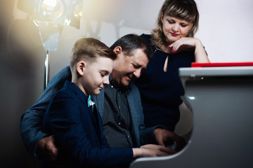 Family playing on the piano. Father and mother teaches son to play a musical instrument