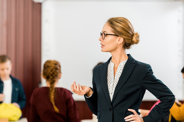 young female teacher in eyeglasses looking away while schoolkids standing behind