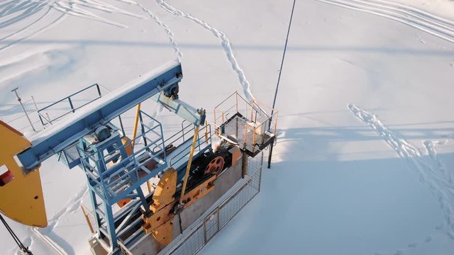 aerial view of pumpjack on oil well in snowy field in winter day, camera is moving around, extraction of petroleum