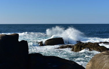 Big waves splashing against the rocks. Blue sea with white foam, sunny day. Galicia, Spain.