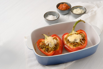 stuffed red bell pepper with cheese au gratin in a blue casserole dish on a white table, copy space