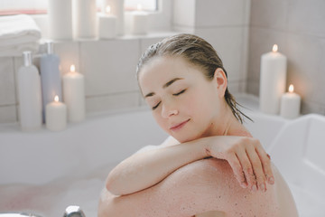 A young beautiful woman uses a body srab in a bath.