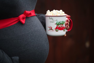 Pregnancy, Christmas and People Concept - close up of Pregnant Woman with Red ribbon over, holding Cup with Hot Coco and  Mushmellow 