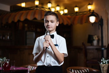 Boy in a white shirt singing into the microphone in a restaurant. baby karaoke.