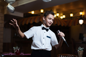 Boy in a white shirt singing into the microphone in a restaurant. baby karaoke.