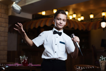 Boy in a white shirt singing into the microphone in a restaurant. baby karaoke.